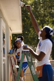 Kansas women’s basketball players Natalie Knight, left, and Carolyn Davis laugh Saturday as they work to add a fresh coat of white paint to the trim of a Habitat for Humanity home located at 1933 Maple Lane. Players and staff members spent part of the morning painting and helping to build a shed for the home and its soon-to-be owners, Hameed Yusuf, his wife Asikat Hameed and their children.
