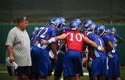 Head coach Charlie Weis walks past as quarterback Dayne Crist pulls the offense into the huddle during practice on Thursday, Aug. 2, 2012.