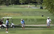 A golfer chips onto a green Wednesday at Lawrence Country Club, as a club employee waters a green in the background. The club has started charging its members a special assessment to help pay its water bill.
