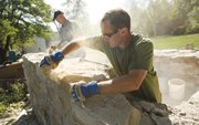 Bryan Murray, lead carpenter with Rockhill and Associates, works in a cloud of dust as he and Doug Callahan, on-site supervisor, back, work to remove stones from an old one-room jailhouse Friday behind Constitution Hall in Lecompton. The jail, which is made of an estimated 1,200 pieces of limestone, is being moved 144 feet to the east and closer to Constitution Hall.
