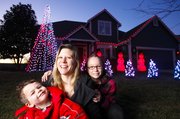 Lawrence mother Stephanie Fisher is pictured with her two children, Noah, 4, and Kaitlyn, 10, in front of their home at 909 Stonecreek Drive. Fisher and her husband, Kent, have put up their Christmas display for years, but this year they’ve included an option for passersby to show their appreciation by donating to charity. Those choosing to do so can text “justfood” to 80888 to make a $10 donation to the food bank.