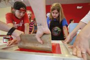 Jessica McClanahan, 13, left, and Katy Walters, 12, apply pressure as ink is pulled across the screen during a screenprinting workshop on Friday, June 21, 2013, at the Lawrence Public Library. Teens attending the activity made t-shirts and learned about screenprinting.