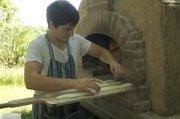Colin Busby scores the top of a baguette before placing it inside the wood-fired
oven he built at his parents' home near Vinland.