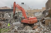 A worker with Midland Wrecking Demolition, of Kansas City, Kan., sprays water to keep the dust down as a large excavator tears down Burt Hall on the Kansas University campus Monday, Aug. 5, 2013. Burt Hall was constructed in the late 1950s and was housed radiation and nuclear engineering programs at KU. The building is being demolished as part of an expansion of KU's School of Engineering.