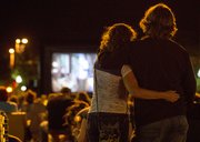A couple stands in the middle of Massachusetts Street Thursday evening as they watch the 1980s movie, The Goonies, on a large, portable movie screen set up at 11th and Massachusetts Streets.