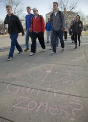 Kansas University students pass by one of several chalk messages on campus Tuesday addressing the issue of allowing concealed carry permit holders to have guns on campus. The messages and a forum were organized by the KU Chapter of Young Americans for Liberty, whose members wore empty holsters Tuesday to protest the ban of guns on campus.