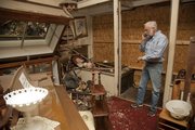 Gary Strong, owner of Strong's Antiques, talks on the phone with a insurance adjuster as he's surrounded by broken items. A Dec. 7 crash sent the motor of the car through the front window of his store, causing significant damage.