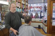 Jon Amyx cuts the hair of customer Randy Wright at the Downtown Barber Shop while three young women look over hair products displayed in the window.
