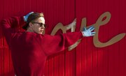 VanGo artist Drew Sheppard holds a stencil in place of the word "love" on the front of the "love" garage on Mississippi Street across from Memorial Stadium Sunday afternoon. For many years, the garage was painted red with the word "love" scrolled across it. However, this past June, the garage was painted over blue. The team from VanGo took old photographs of the garage and aim to recreate the old "love" garage while adding in a bit of their own flair.