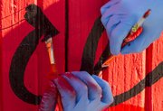 VanGo artists work on painting the "love" garage on Mississippi Street across from Memorial Stadium Sunday afternoon. For many years, the garage was painted red with the word "love" scrolled across it. However, this past June, the garage was painted over blue. The team from VanGo took old photographs of the garage and aim to recreate the old "love" garage while adding in a bit of their own flair.
