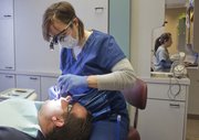 Mary Marshall, a registered dental hygienist at Douglas County Dental Clinic, checks the teeth of her brother and patient Gary Marshall on Thursday. A hearing will soon be held in the state legislature for an anti-fluoride bill that would require municipalities that fluoridate their water, which includes Lawrence, to notify citizens that fluoride can reduce the IQ of children. Oral health advocates are fighting back.