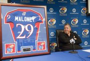 Kansas University football coach Charlie Weis glances as a framed KU jersey in memory of Andre Maloney, a Shawnee Mission West senior who had orally committed to Kansas before he suffered a stroke and died in a game this past October.