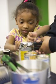 Five-year-old Leah Anderson, of Lawrence, gets some assistance opening cans of food during a cooking class held Tuesday at Just Food, 1000 E. 11th St.