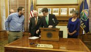 Governor Sam Brownback looks at a petition delivered by Aaron Estabrook, front left, a school board member from Manhattan, Kan., before signing a school finance bill that will increase funding to schools but which also contains some controversial policy changes, Monday, April 21, 2014 in his ceremonial office at the Kansas Statehouse in Topeka, Kan. With Brownback are House Appropriations chairman Gene Suellentrop, left and partially obscured, R-Wichita, House Speaker Ray Merrick, R-Stillwell and Senate President Susan Wagle, R-Wichita. Estabrook had asked Brownback not to sign the bill, which has been criticized by teacher groups because it repeals tenure for teachers.