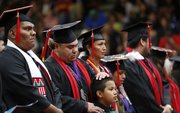 Haskell graduate Jaime Scott, Confederate Tribes of Warm Springs, Lawrence, holds his son Demarcus, 8, in front of him before receiving his diploma on Friday at Coffin Sports Complex.