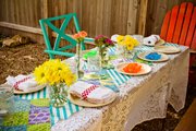 Putting together a couple of card tables, then covering them with a tablecloth or two, should provide enough seating for at least 15 people. The tables are decorated with flowers and tea-light candles in jars.