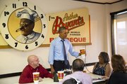 President Barack Obama picks up a souvenir cup while meeting with four Kansas City residents who wrote him letters, over dinner at Arthur Bryant’s Barbeque restaurant Tuesday in Kansas City, Mo. Clockwise from left are Victor Fugate, the president, Becky Forrest, Valerie McCaw, and Mark Turner.