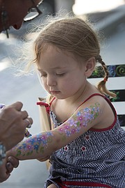 Two-year-old Leona Richardson, of Lawrence, watches as she has flowers painted on her arm at the Sidewalk Sale in downtown Lawrence on Thursday, July 21, 2016.