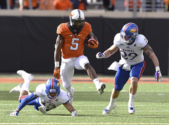 Oklahoma St running back Justice Hill (5) runs between Kansas corner back Hasan Defense (13) and linebacker Joe Dineen Jr. (29) during the second half of a NCAA college football game in Stillwater, Okla., Saturday, Nov. 25, 2017. Hill led Oklahoma St rushing with 58 yards in the 58-17 win over Kansas.