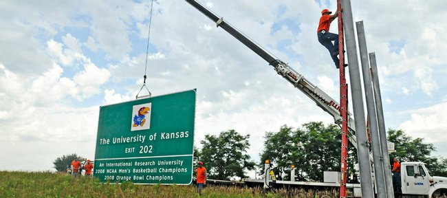 Workers from the Kansas Turnpike Authority erect a road sign announcing the exit for Kansas University two miles east of the East Lawrence exit on I-70. The new sign, which lays claim to Kansas' status as an international research university, 2008 NCAA Men's Basketball Champions and 2008 Orange Bowl Champions, was installed on Wednesday at mile marker 207.