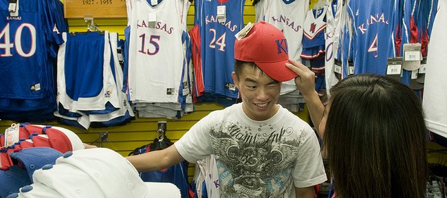 Kansas University freshman Travis Young, Garden City, winces as his friend Kim Nguyen, also a Garden City freshman, pulls a KU hat down on his head Wednesday at Jayhawk Bookstore. Through the end of June, KU had received $626,000 in royalties from sales of licensed merchandise connected with KU's national basketball championship, a record haul for such a title.