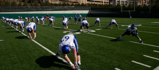 Offensive players on Kansas University’s football team stretch prior to the Jayhawks’ first practice Sunday on the KU practice fields. After having worked out twice without pads, the Jayhawks will don pads today for the first time this spring.
