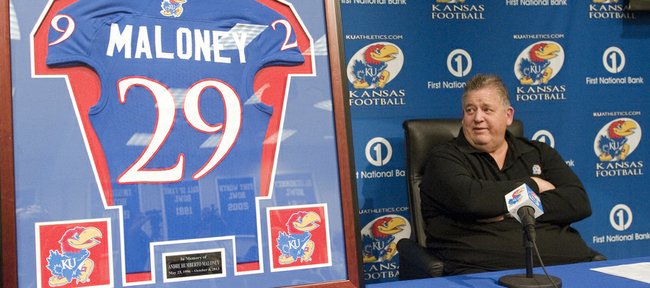 Kansas University football coach Charlie Weis glances as a framed KU jersey in memory of Andre Maloney, a Shawnee Mission West senior who had orally committed to Kansas before he suffered a stroke and died in a game this past October.
