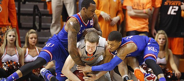 Kansas forward Cliff Alexander, left, and guard Frank Mason III collapse on top of Oklahoma State forward Mitchell Solomon (41) as they compete for control of a loose ball during the first half on Saturday, Feb. 7, 2015 at Gallagher-Iba Arena.