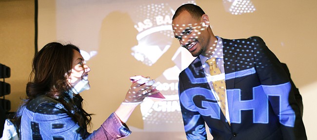 Kansas men’s basketball junior Perry Ellis, right, illuminated with a projected logo of the Jayhawks' 11 straight conference championships, is shown a photograph by an attendee at the team's postseason awards banquet Monday April 13, 2015. Ellis received the Danny Manning - Mr. Jayhawk award at the banquet. 