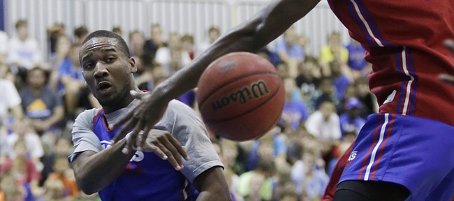 Kansas guard Wayne Selden Jr., left, passes beneath the basket and the defense of Carlton Bragg during a practice game between current and former KU players Wednesday, June 17, 2015 at a Bill Self Basketball Camp. 