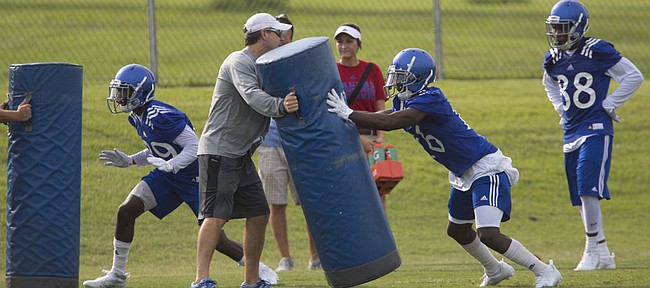 Kansas offensive coordinator Rob Likens holds a pad upright as receivers DeAnte Ford, left, and Steven Sims Jr. practice coming off a block during the first day of practice on Thursday, Aug. 6, 2015 at the fields south of Anschutz Pavilion.