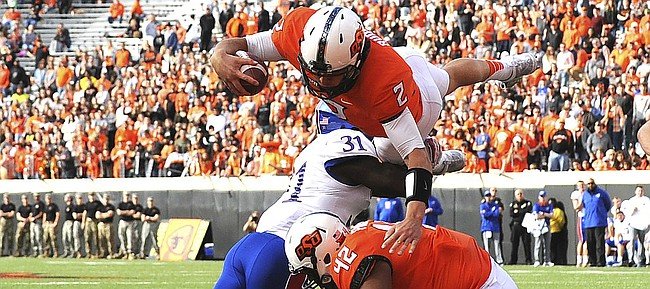 Oklahoma St quarterback Mason Rudolph (2) jumps over Kansas linebacker Osaze Ogbebor (31) and Oklahoma St tight end Sione Finefeuiaki for a touchdown during the third quarter of an NCAA college football game between Kansas and Oklahoma St in Stillwater, Okla., Saturday, Nov. 25, 2017. Rudolph ran for 2 touchdowns in the 58-17 win over Kansas.