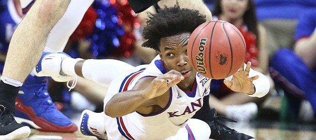 Kansas guard Devonte' Graham (4) tosses a ball from the floor as Washington forward Sam Timmins (33) hovers over during the second half, Wednesday, Dec. 6, 2017 at Sprint Center.