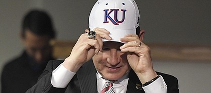 Newly hired University of Kansas football coach Les Miles puts on a KU hat during a press conference Sunday, Nov. 18, 2018, at Hadl Auditorium.