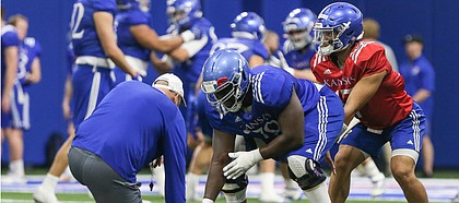 Kansas offensive line coach Luke Meadows gets down as he works with lineman Hakeem Adeniji as he snaps to quarterback Miles Kendrick on Thursday, April 4, 2019 at the indoor practice facility.