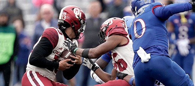 Oklahoma running back Kennedy Brooks, center, hands the ball off to quarterback Caleb Williams, left, as he is being tackled by Kansas linebacker Rich Miller during the second half of an NCAA college football game Saturday, Oct. 23, 2021, in Lawrence, Kan. Oklahoma won 35-23. (AP Photo/Charlie Riedel)


