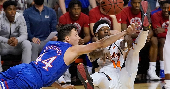 Oklahoma State guard Bryce Williams (14) passes in front of Kansas forward Mitch Lightfoot (44) in the first half of an NCAA college basketball game Tuesday, Jan. 4, 2022, in Stillwater, Okla. (AP Photo/Sue Ogrocki)
