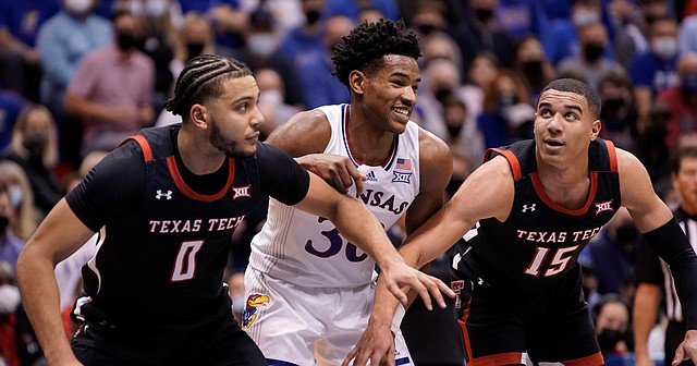 Kansas guard Ochai Agbaji (30) flashes a smile as he works for position against Texas Tech forward Kevin Obanor (0) and Texas Tech guard Kevin McCullar (15) during the first half on Monday, Jan. 24, 2022 at Allen Fieldhouse.