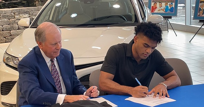 Kansas guard Remy Martin, right, signs the paperwork on his NIL partnership with Crown Toyota as owner Miles Schnaer looks on at the dealership on Thursday, Oct. 28, 2021. 