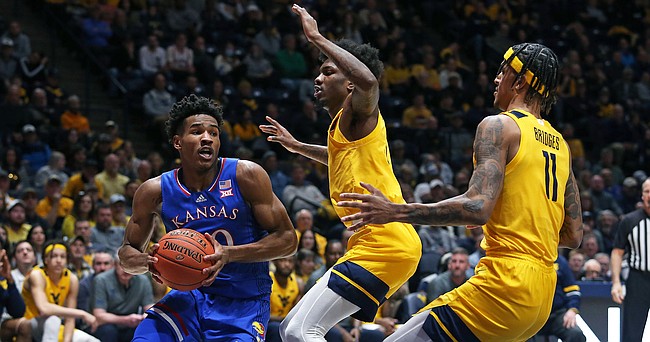 Kansas guard Ochai Agbaji, left, is defended by West Virginia guard Kedrian Johnson, center, and forward Jalen Bridges during the first half of an NCAA college basketball game in Morgantown, W.Va., Saturday, Feb. 19, 2022.