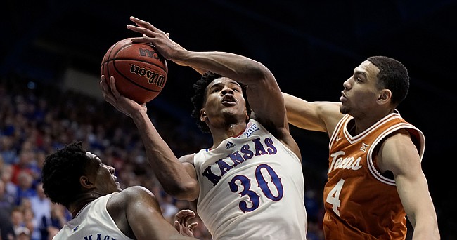 Kansas guard Ochai Agbaji (30) adjusts his shot as he is fouled by Texas forward Dylan Disu (4) during overtime on Saturday, March 5, 2022 at Allen Fieldhouse. At left is Kansas forward David McCormack (33). The Jayhawks defeated the Longhorns, 70-63 to win a share of the Big 12 conference title.