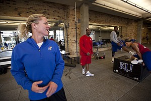 Andrea Hudy turns over her shoulder to laugh with players Thomas Robinson, Niko Roberts and assistant strength and conditioning coach Glenn Cain during a workout session. Nick Krug/Journal-World Photo