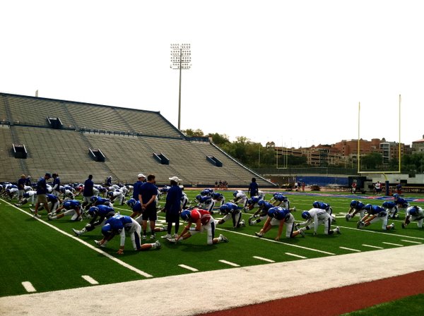 The KU football team runs through pre-game stretches just as it would on Saturdays this fall. The season opener is now just two weeks away. 
