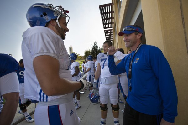 Kansas head football coach Clint Bowen laughs with senior offensive lineman Pat Lewandowski as the team gathers outside the football complex to make their way to the field together on Wednesday, Oct. 22, 2014.
