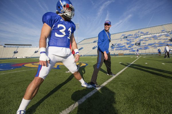 Kansas head football coach Clint Bowen laughs with senior defensive captain Ben Heeney as Heeney leads the team in stretching at the beginning of practice on Wednesday, Oct. 22, 2014.