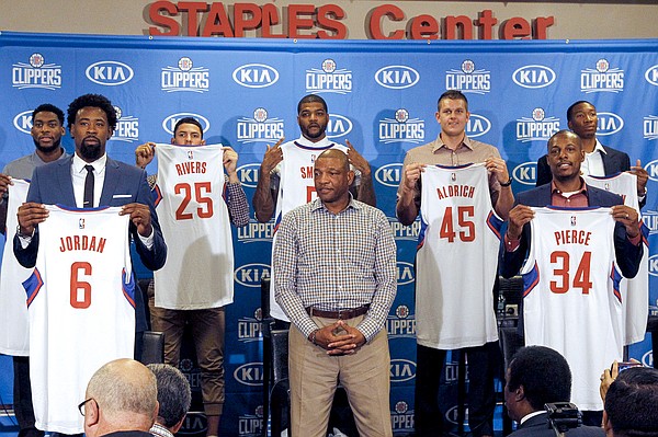 Los Angeles Clipper, head coach Doc Rivers, center, poses team players, from left, Branden Dawson, 22, DeAndre Jordan, 6, Austin Rivers, 25, Josh Smith, 5, Cole Aldrich, 45, Paul Pierce, 34, and Wesley Johnson, 33, far right, at at a news conference in Los Angeles on Tuesday, July 21, 2015. The Clippers managed to keep DeAndre Jordan after he changed his mind about his verbal commitment to Dallas Mavericks. They offered everything he wanted, including a fresh start and a bigger offensive role. When Jordan thought about it a little more, the craziest free-agent recruitment story in recent NBA history ended with him back on the Los Angeles Clippers. (AP Photo/Nick Ut)
