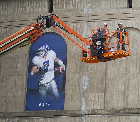 Workers in a cherry picker come down next to a banner of former Kansas linebacker Nick Reid, while doing some exterior work on Memorial Stadium, Monday, Aug. 7, 2017.