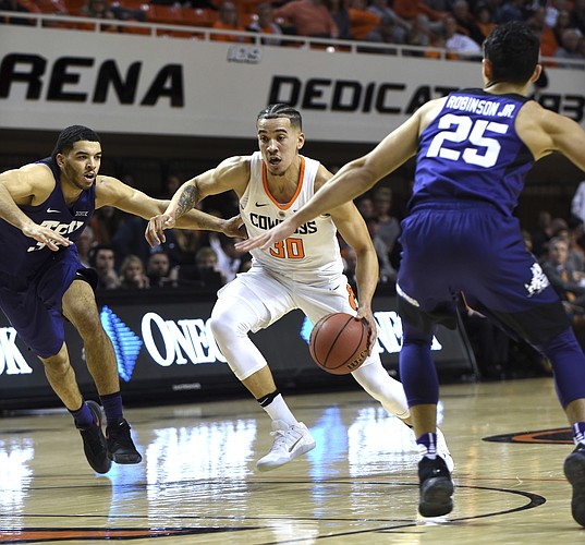 Oklahoma State guard Jeffrey Carroll, center, drives the ball between TCU guards Kenrich Williams, left, and Alex Robinson in the first half of a NCAA college basketball game in Stillwater, Okla., Tuesday, Jan. 30, 2018.