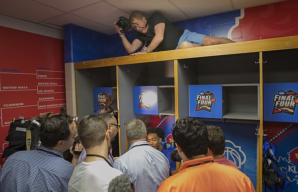 In a tightly-packer locker room, Kansas Athletics photographer Jeff Jacobsen steadies himself above the locker of Devonte' Graham to get a fisheye view as media members talk with Graham on Thursday, March 29, 2018 at the Alamodome in San Antonio.