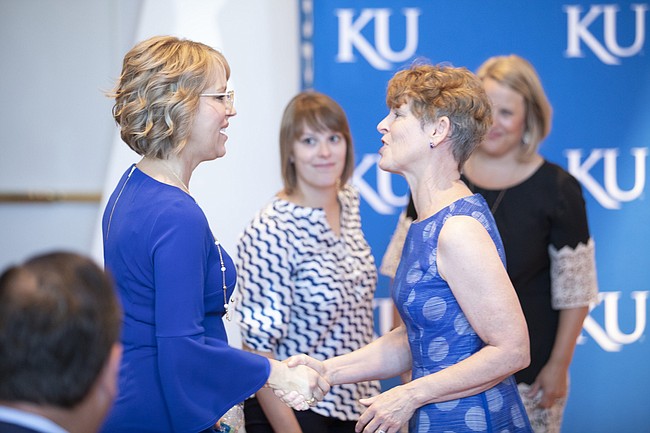 Fanny Long, wife of new University of Kansas athletic director Jeff Long, left, is greeted by Susan Girod, wife of University of Kansas Chancellor Douglas Girod as the two sit for Jeff Long's introductory news conference on Wednesday, July 11, 2018 at the Lied Center Pavilion.